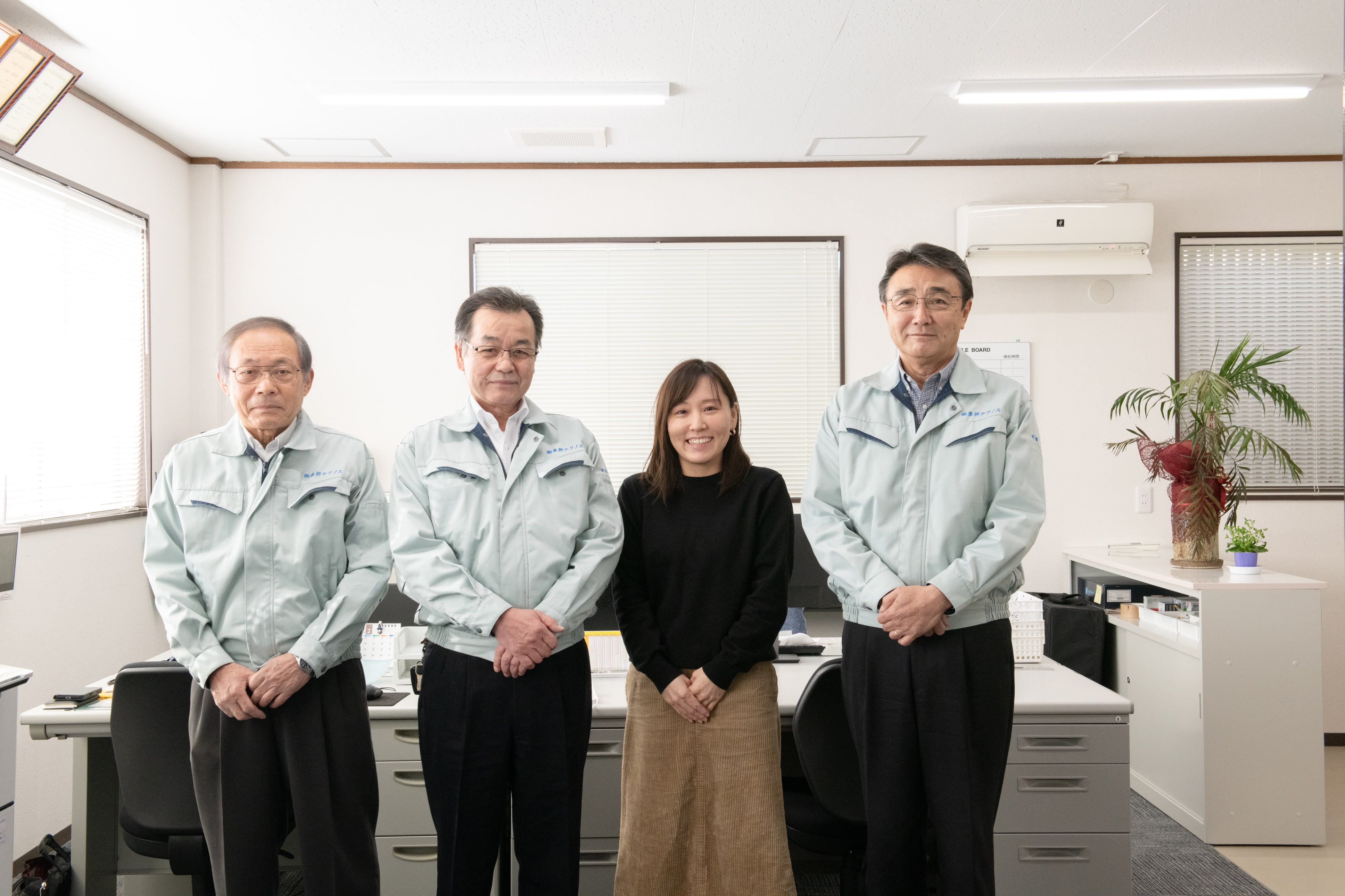 新入社員が、東邦テクノスの代表 望月英男、役員と一緒に並んで事務所で立っている写真